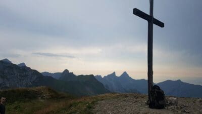 A backpack rests at the foot of a cross on an overlook.